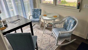 A cozy room with a dining table, two chairs, a small round table with a book, and a rocking chair.