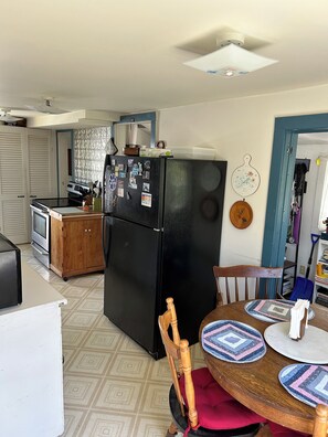 Una cocina compacta con un refrigerador negro, armarios de madera y una zona de comedor con una mesa redonda y sillas.