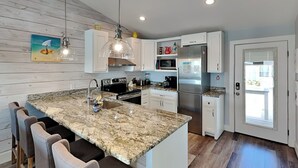 A modern kitchen with a granite island, bar stools, stainless steel appliances, and a wooden floor.
