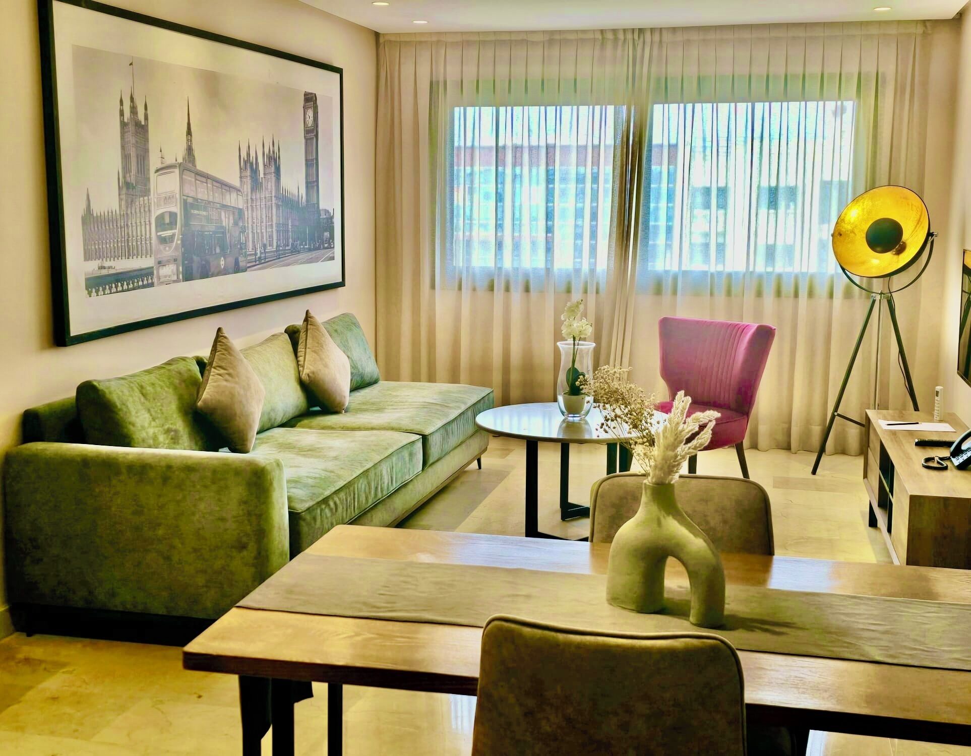 Un salon avec un canapé vert, un fauteuil rose, une table ronde et une lampe.