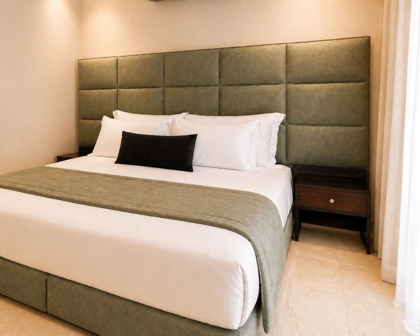 A neatly made bed with a tufted headboard, a bedside table with a drawer, and a light-colored carpet.