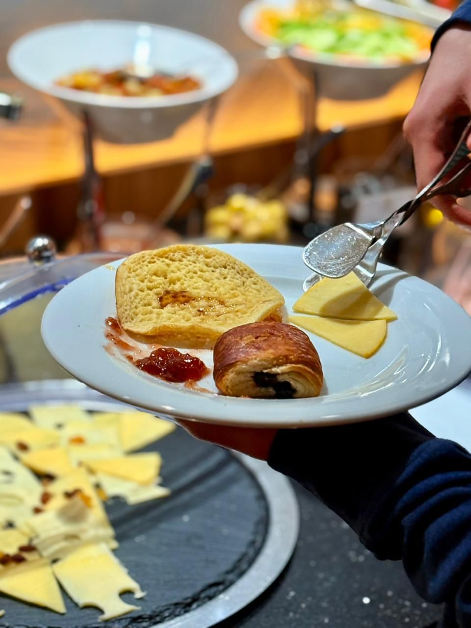 A plate with food items, a spoon, and a person holding the plate.