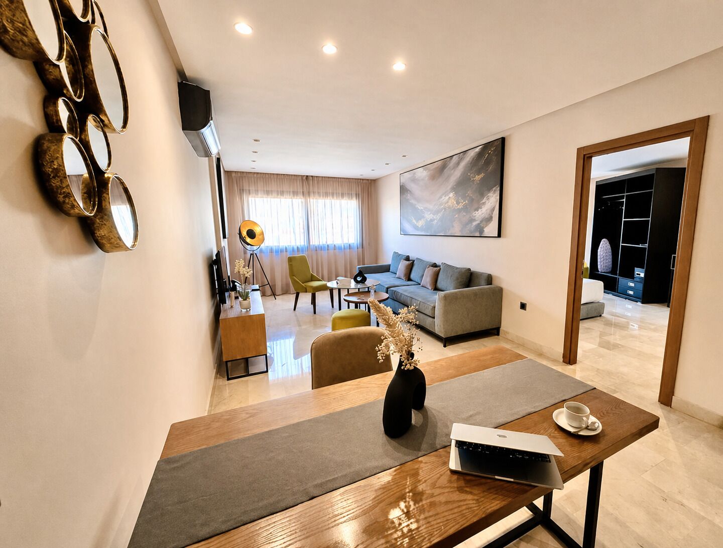 Una sala de estar moderna con un sofá, una mesa de centro y un comedor con una computadora portátil y una taza.