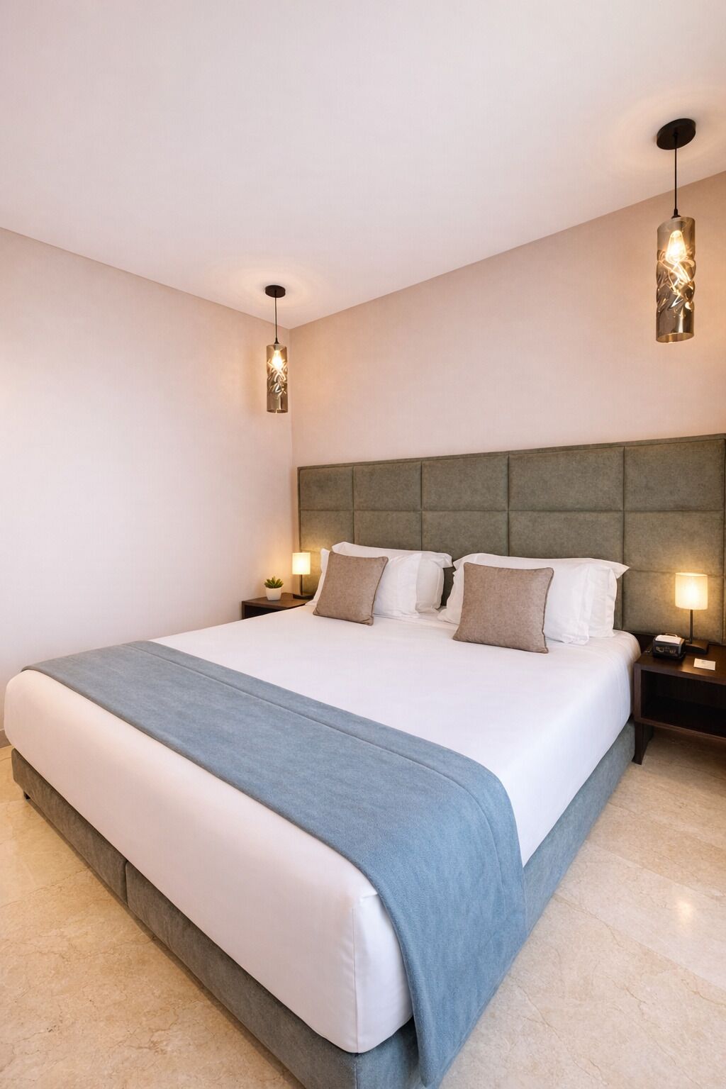 Una habitación de hotel moderna con una cama grande, dos mesitas de noche con lámparas y un aplique decorativo sobre la cama.