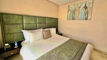 A hotel room with a large bed, a green headboard, a nightstand with a water bottle, and a painting on the wall.