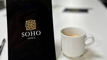 A hotel reception area with a black sign displaying the hotel name, a white mug with coffee, and a water bottle on a counter.