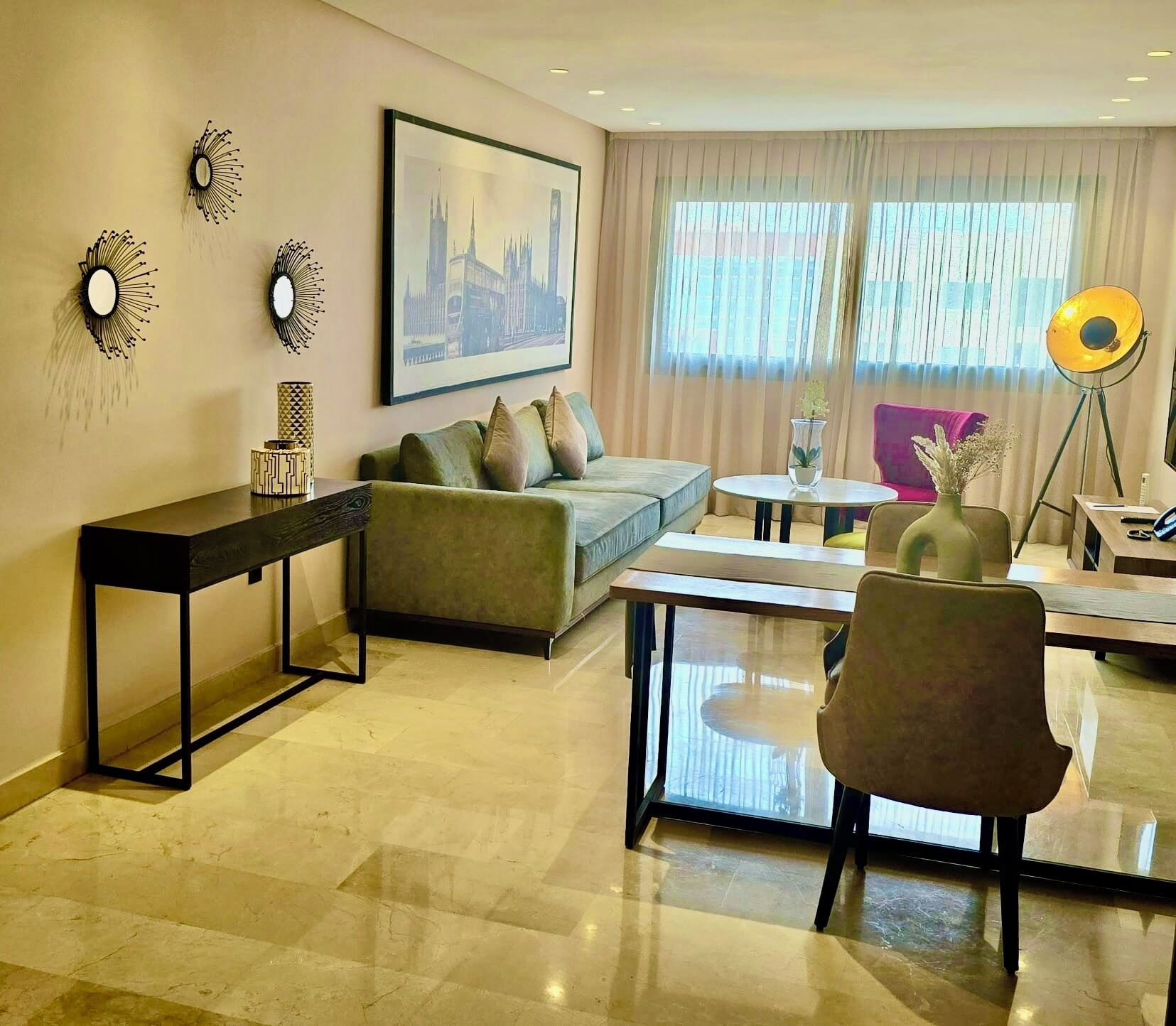 Una sala moderna con un sofá, una mesa de centro y un mueble para televisión. Hay un cuadro en la pared y una lámpara con trípode.