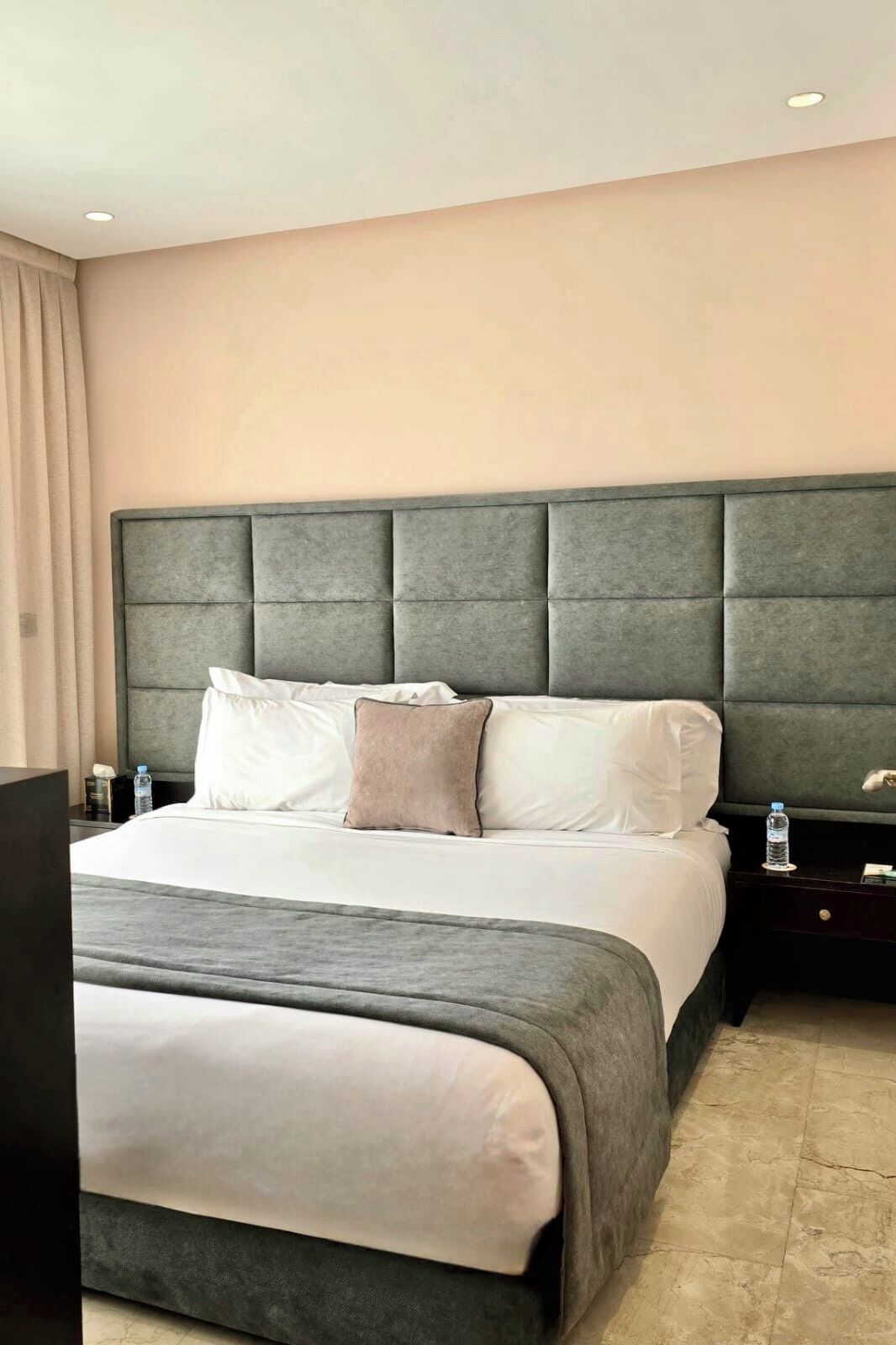 A hotel room with a large bed, a headboard, a nightstand, and a water bottle.
