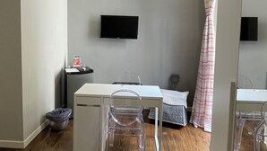 A room with a wooden ceiling, a white desk with a chair, a television on the wall, and a large mirror. - Anima Partenopea (Naples)