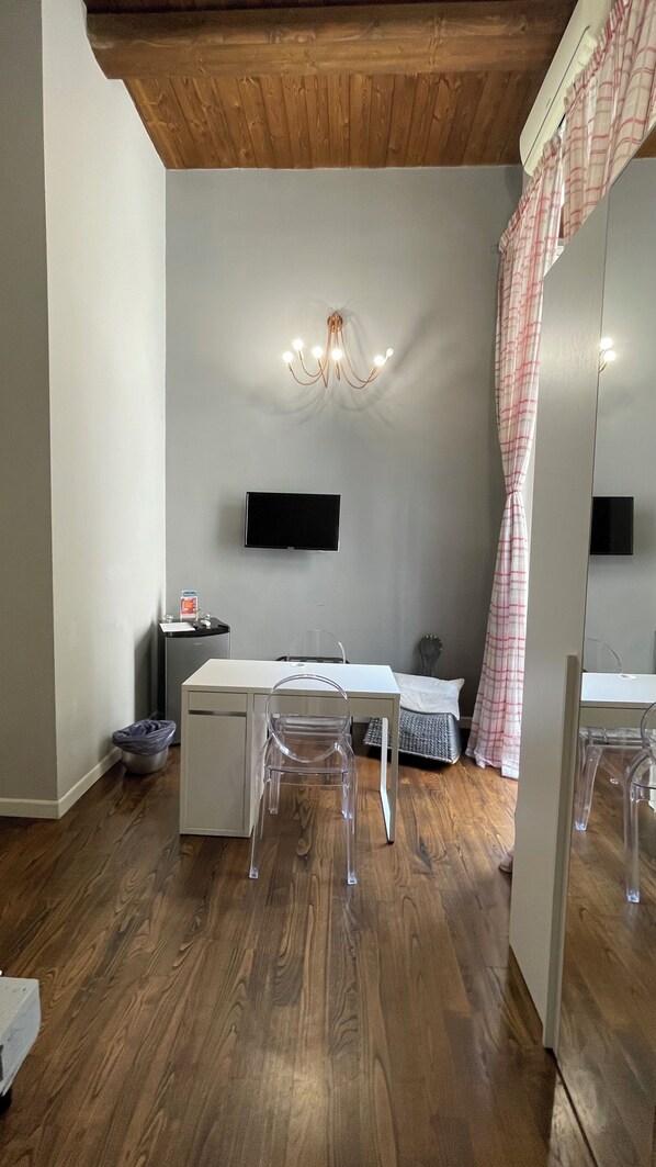 Ein Zimmer mit Holzbalkendecke, einem weißen Schreibtisch mit Stuhl, einem an der Wand montierten Fernseher und einem großen Spiegel.