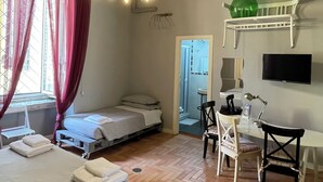 A room with two beds, a desk, a chair, a television, and a chandelier. - Anima Partenopea (Naples)