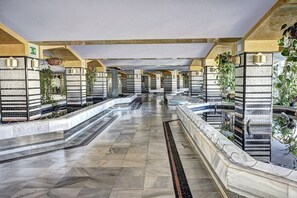 A hotel corridor with tiled floors, hanging plants, and a view of the sea.