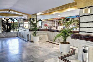 A spacious lobby with a marble floor, a reception desk, and potted plants.