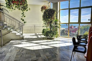 A spacious indoor area with a marble floor, a staircase, and large windows offering a view of the city.