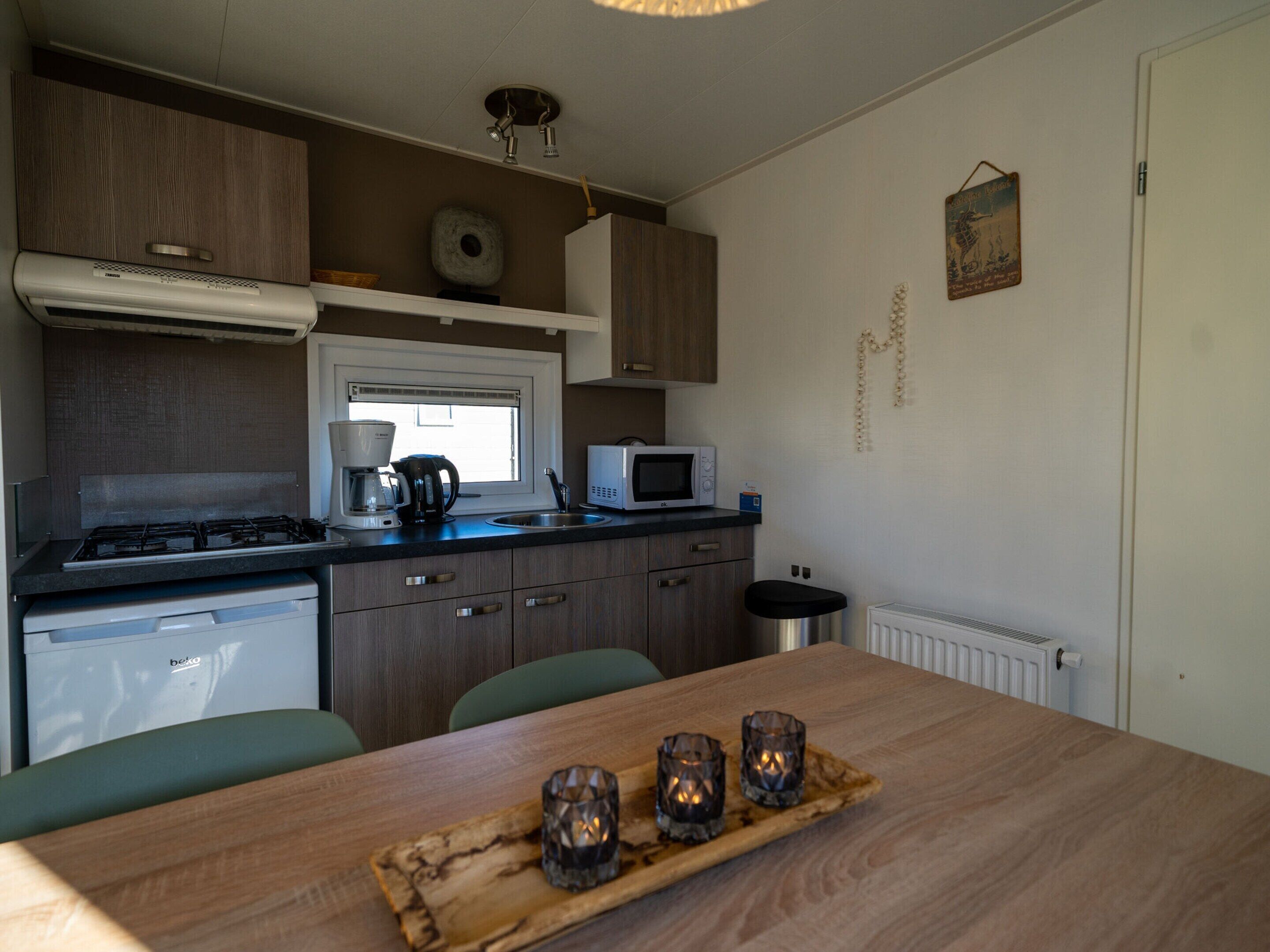 Cocina compacta con estufa a gas, microondas y cafetera. Hay una mesa de madera con una bandeja que contiene velas.