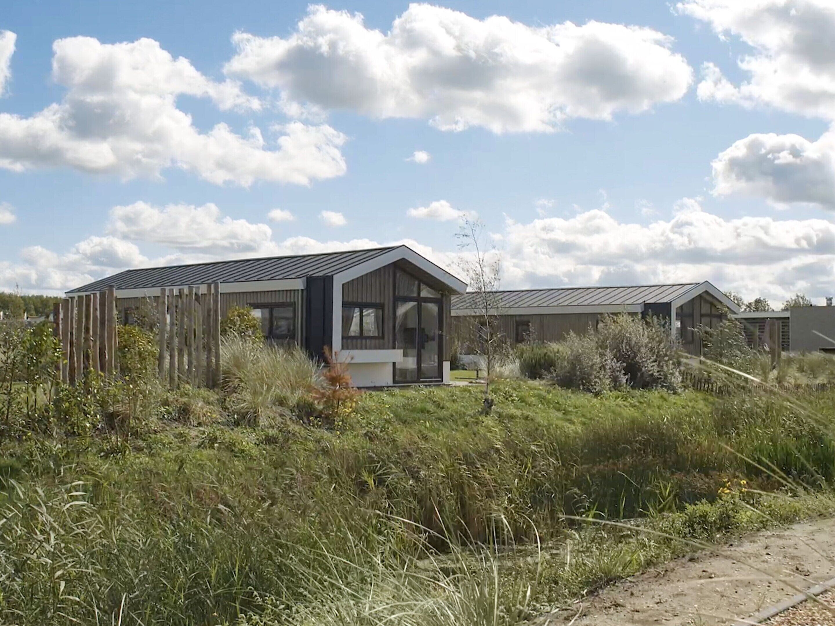 A modern house with a large glass door and a sloped roof, surrounded by tall grass and a clear sky.