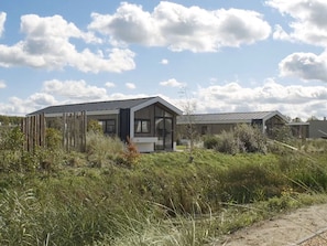 A modern house with a large glass door and a sloped roof, surrounded by tall grass and a clear sky. - Well-maintained Chalet With Terrace (Hellevoetsluis)