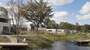 Overlooking a serene water body, this house features a flat roof and large windows, with a wooden deck and bench offering a peaceful retreat.