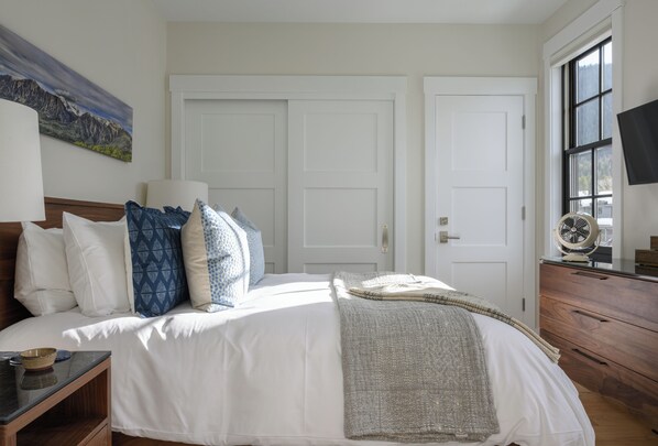 A bedroom with a bed, nightstands, a dresser, a television, and a painting on the wall.
