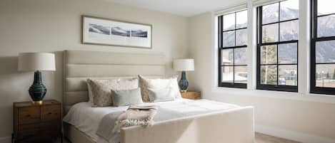 A bedroom with a large bed, two bedside tables, a window with a mountain view, and a ceiling light fixture.