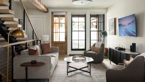A modern living room with a staircase, a sofa, a coffee table, and a television. - Academy Place | Yarrow (Crested Butte)