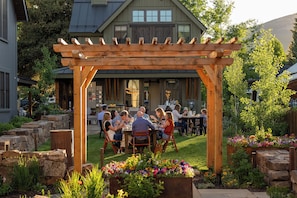 A wooden pergola with a group of people dining at an outdoor table. - Wild Iris at Academy Place (Crested Butte)