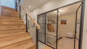 A staircase with wooden steps and metal railings leading to a bedroom with a bed, a ladder, and a view of the outdoors.