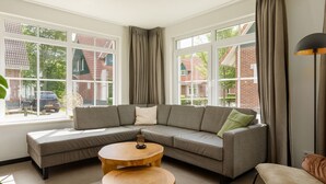 A modern living room with a sectional sofa, two wooden side tables, and large windows with curtains. - Holiday Home in Bad Bentheim With Sauna (Bad Bentheim)