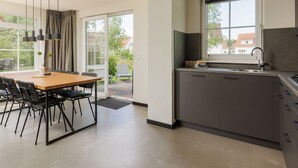 A modern kitchen with a large window, a dining area with a wooden table and black chairs, and a sliding glass door leading to an outdoor area. - Holiday Home in Bad Bentheim With Sauna (Bad Bentheim)