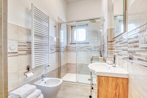 A modern bathroom with a glass shower enclosure, a bidet, and a vanity with a mirror. - Lanterne Luxury Apartments (Borghetto Santo Spirito)