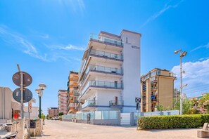 A multi-story hotel with balconies, a clear sky, and a street with parked cars. - Lanterne Luxury Apartments (Borghetto Santo Spirito)