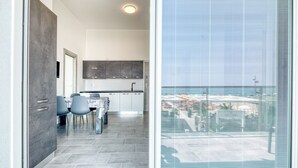 Une cuisine moderne avec des meubles gris, un coin repas avec des chaises bleues et une grande fenêtre donnant sur la mer.