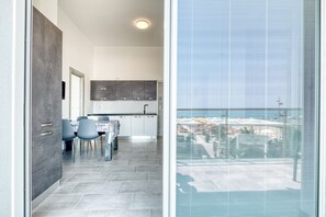 Una cocina moderna con armarios grises, un comedor con sillas azules y un amplio ventanal con vistas a la costa.