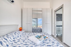 A modern bedroom with a bed, a nightstand, a lamp, and a view of the city through a large window. - Lanterne Luxury Apartments (Borghetto Santo Spirito)