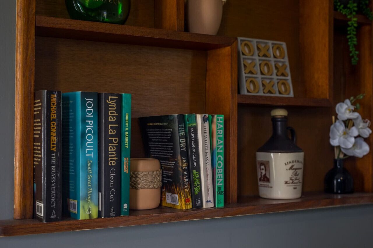 A wooden shelf with books, a ceramic mug, and a small vase with flowers.