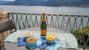 Una mesa dispuesta con una botella de champán, dos copas y fuentes de aperitivos en una terraza con vistas a un lago y montañas al fondo.