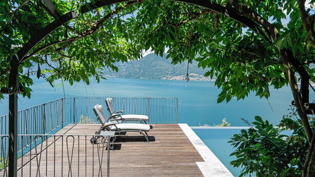 Una terraza de madera con dos sillones de relax con vista a un cuerpo de agua y una montaña distante.