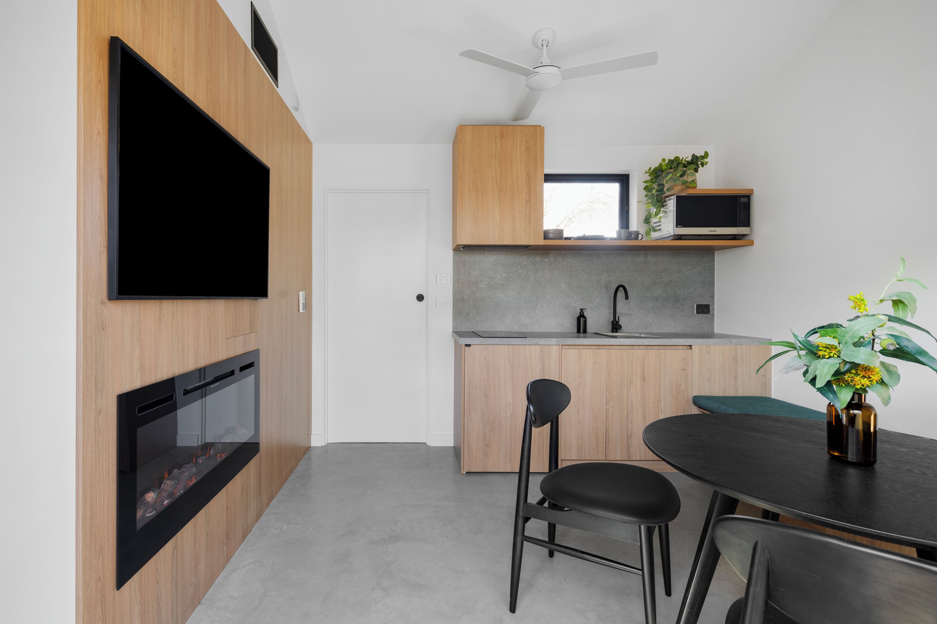 A modern kitchen with a flat-screen TV, built-in oven, microwave, and sink. There is a dining area with a table and chairs.