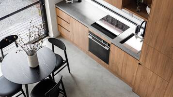 A modern kitchen with wooden cabinets, a built-in oven, and a sink. There is a dining table with chairs and a vase with dried flowers.