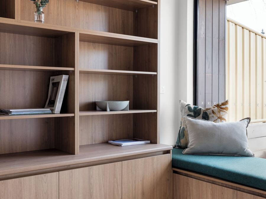 A corner room with a built-in wooden shelving unit, a cushioned bench, and a window with a view.
