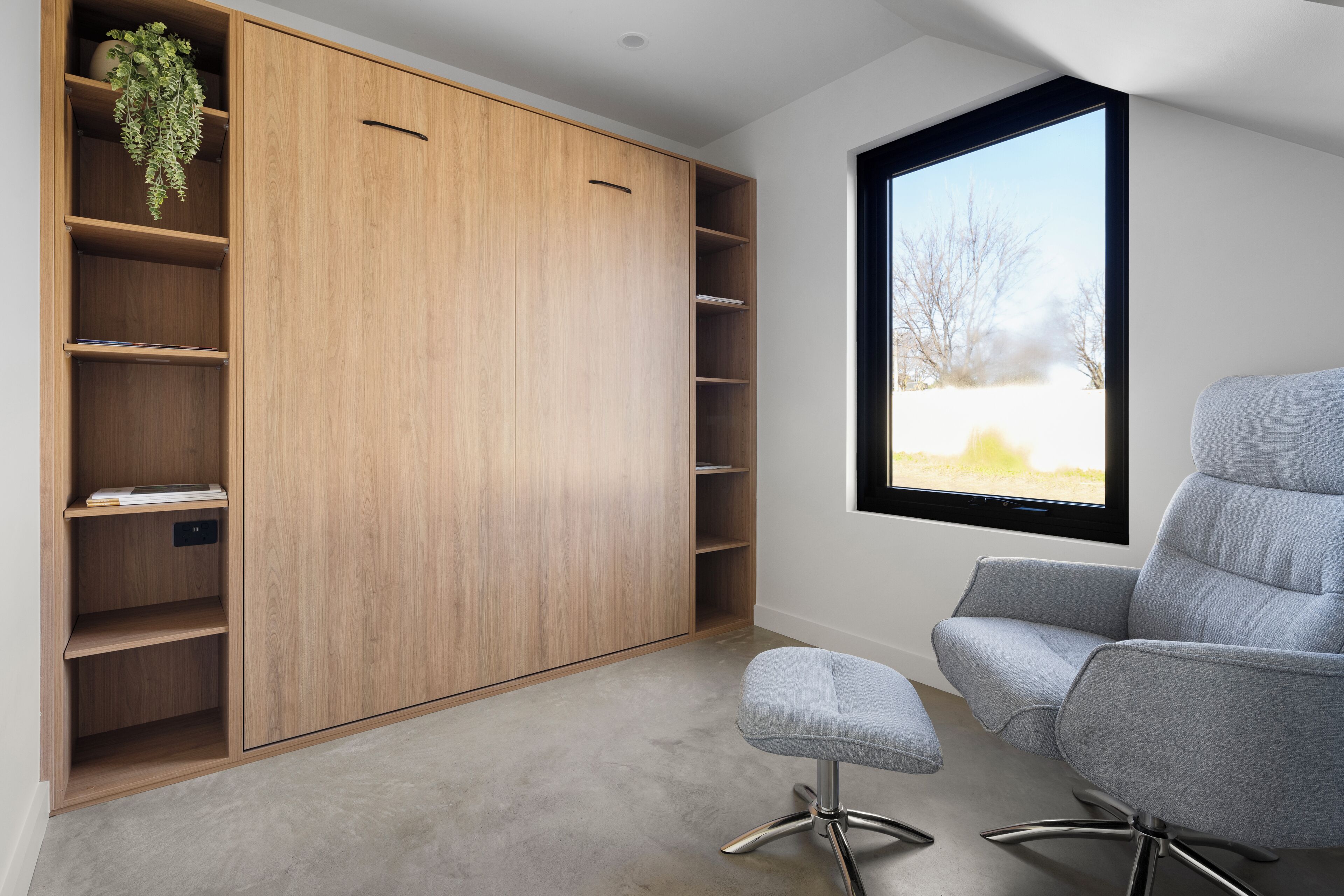 A modern room with a large wooden wardrobe, a grey office chair, and a window with a view of a snowy landscape.