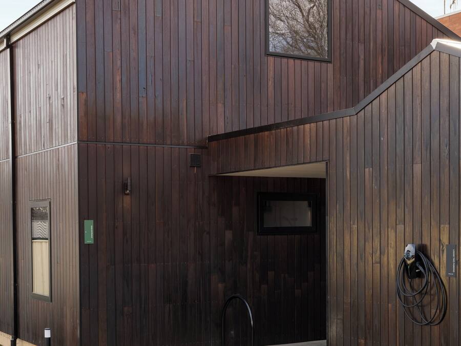Un edificio grande de madera oscura con entrada de hormigón y una ventana pequeña.