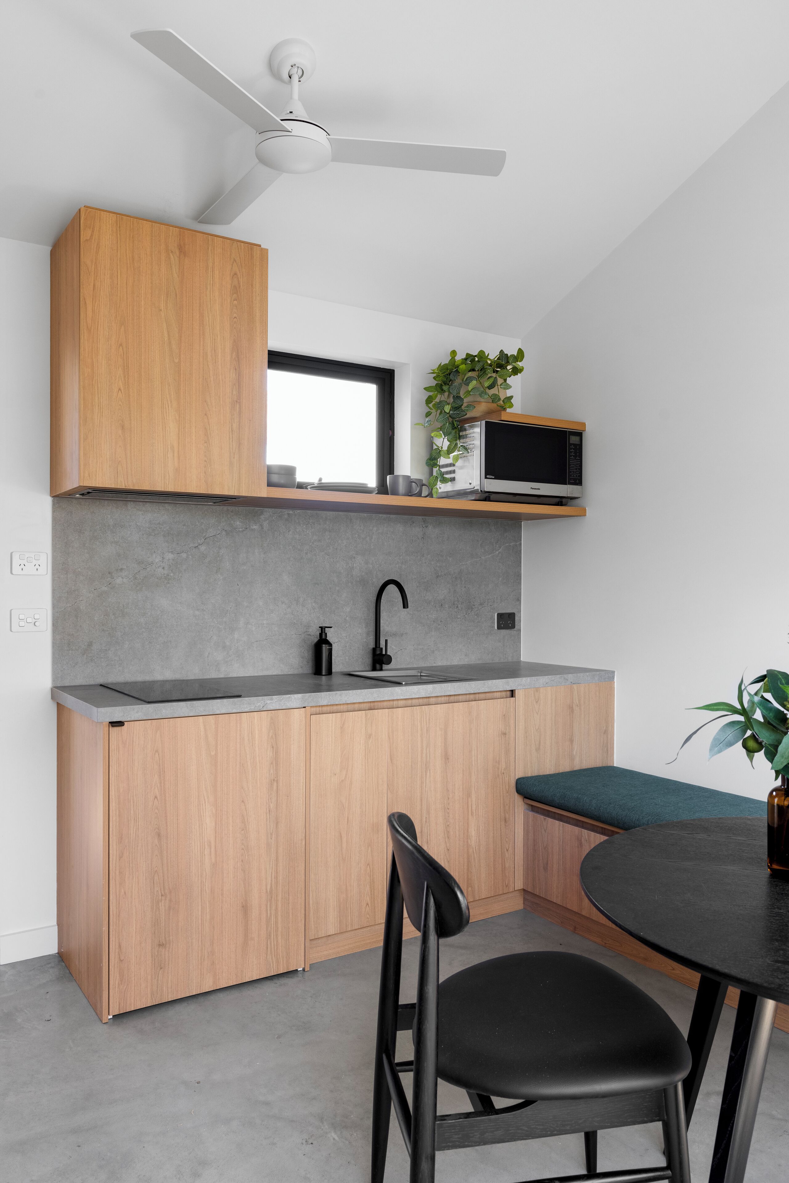 Una cocina compacta con armarios de madera, una encimera gris, un grifo negro, un microondas y un ventilador de techo.