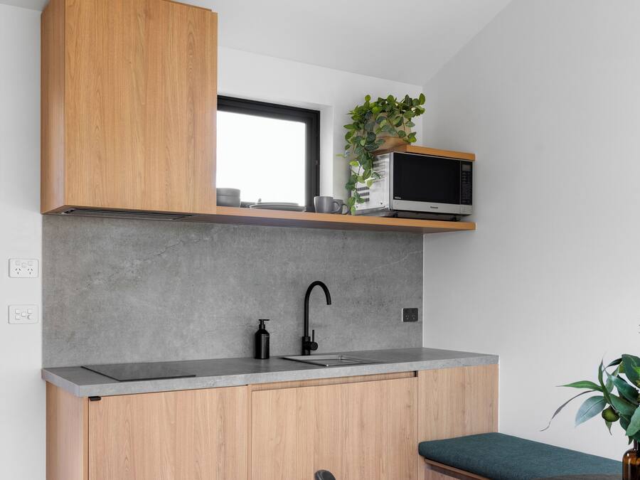 Una cocina compacta con armarios de madera, una encimera gris, un grifo negro, un microondas y un ventilador de techo.