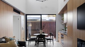 A modern kitchen with a dining area, a black leather couch, and a large TV on the wall. - Bendigo Lodges (Bendigo)
