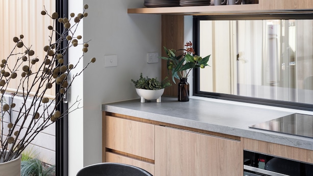 A modern kitchen with wooden cabinets, a stainless steel countertop, and a window overlooking a garden. - Bendigo Lodges (Bendigo)