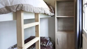 A bunk bed with a white mattress and a wooden headboard, a wooden wardrobe with a handle, and a window with a curtain. - Nice Chalet in a Holiday Park (Arnhem)