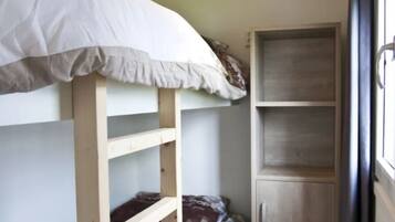 A bunk bed with a white mattress and a wooden headboard, a wooden wardrobe with a handle, and a window with a curtain.