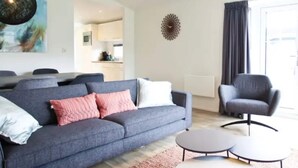 Una sala de estar moderna con un sofá gris, dos mesas redondas de centro, un sillón gris y un comedor al fondo.