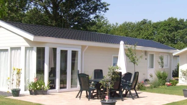A house with a patio area featuring a table and chairs, surrounded by potted plants and a covered seating area. - Nice Chalet in a Holiday Park (Arnhem)